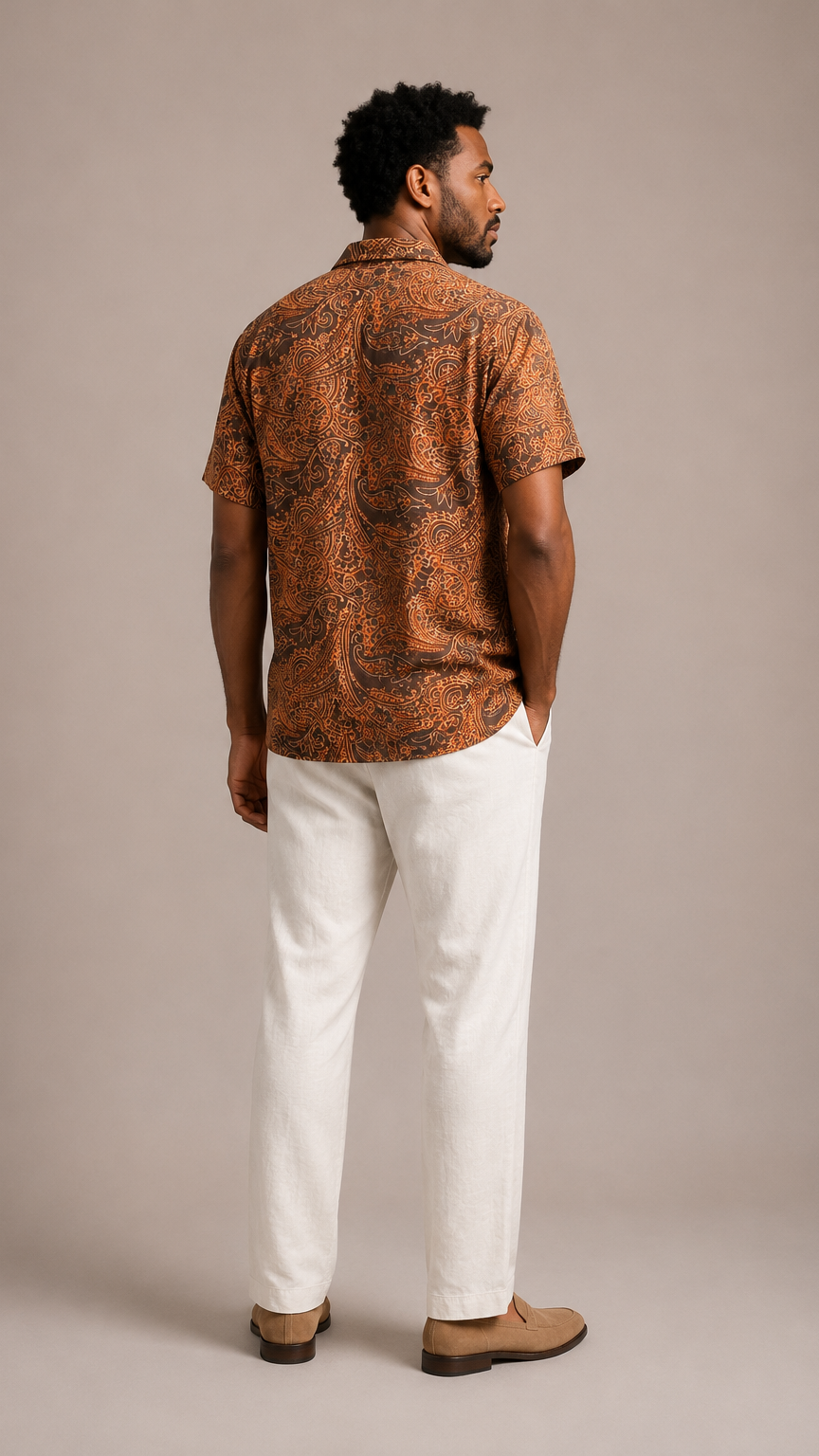 Man wearing a patterned brown shirt and white pants against a beige background