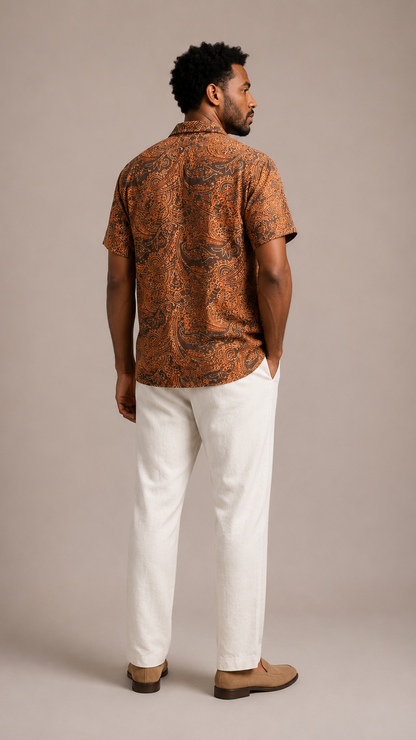 Man wearing a patterned brown shirt and white pants against a beige background